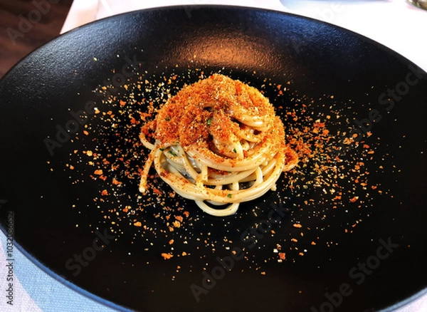 Fototapeta Black plate with portion of spaghetti and toasted bread crumbs