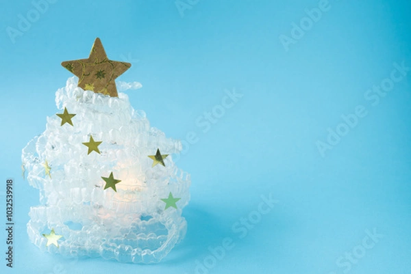 Fototapeta Christmas tree made with clear dental aligners. A Christmas tree made of clear beads and a gold star sits on a blue background. The tree is surrounded by white glitter, giving it a festive and sparkli