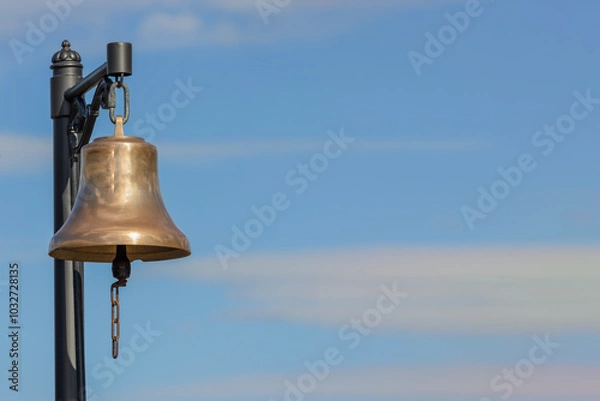 Fototapeta shiny station bell with chain against blue sky with clouds