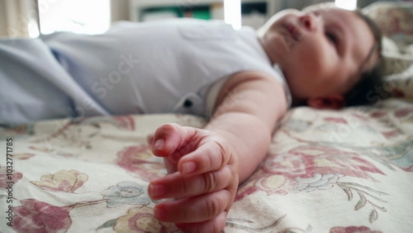 Fototapeta Baby lying comfortably on a patterned blanket, reaching out with one arm. The scene captures the baby’s full body while relaxing in a cozy home setting