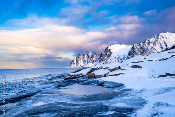 Fototapeta Tungeneset or Devils Jaw mountain on Senja island, Norway in winter. Winter landscape with snowy mountain peaks, fjord waters and ice coast in northern Norway. Scenic view with dramatic sky