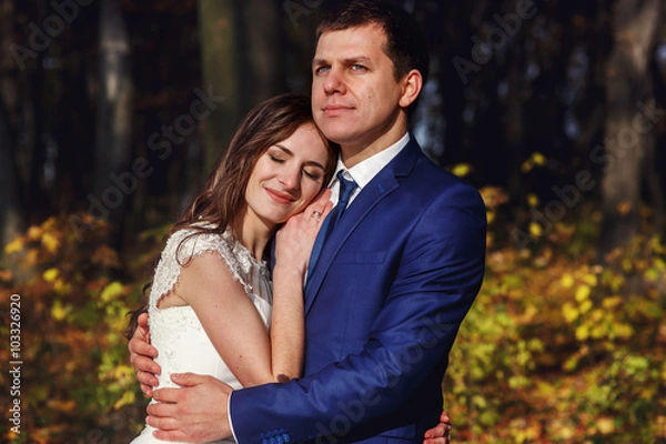 Fototapeta Romantic, happy newlywed couple hugging in autumn park at sunset