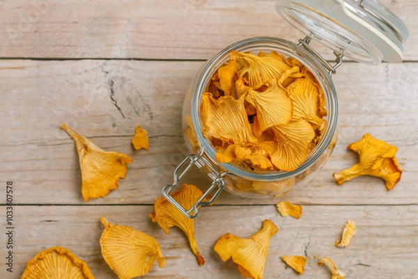 Fototapeta Dried chanterelles in a glass jar on a wooden table. Useful forest mushrooms. Cantharēllus cibārius. Selective focus