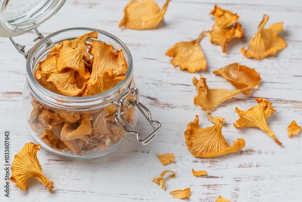Fototapeta Dried chanterelles in a glass jar on a wooden table. Useful forest mushrooms. Cantharēllus cibārius. Selective focus