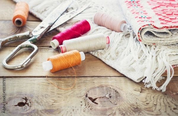 Obraz Scissors, bobbins with thread and needles, striped fabric. Old sewing tools on the old wooden background. Vintage Background