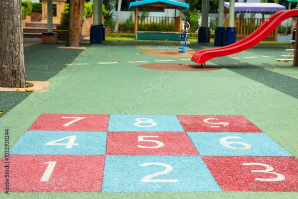 Fototapeta A colorful hopscotch grid sits in empty playground, inviting outdoor fun and physical activity. This vibrant children’s play area promotes fitness and active play of childhood recreation in a park.