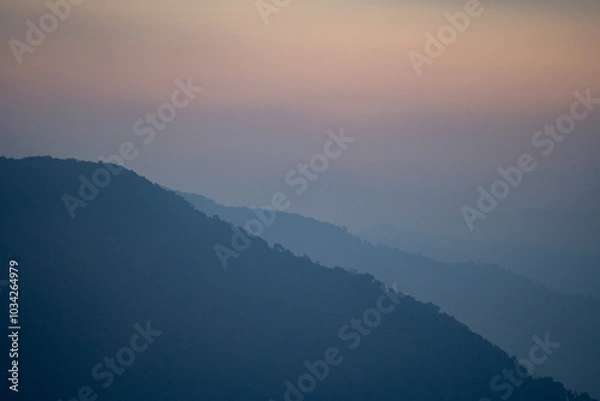 Fototapeta As dawn broke, the mist rose from the vale, revealing a breathtaking landscape where mountains kissed the sky, hills framed the view, and trees danced in the morning fog.