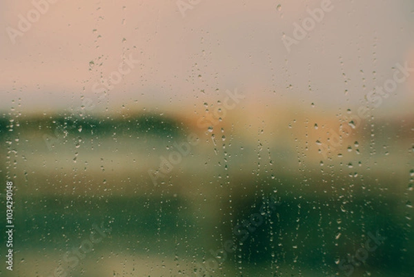 Fototapeta The window glass is covered in a thin layer of water from the rain. A hazy image of the landscape can be seen through it. This forms the backdrop.