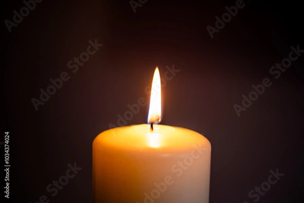 Fototapeta A single candle flame illuminating darkness in a serene indoor setting during evening hours. Baccground for funeral, obituary, in memoriam with copy space