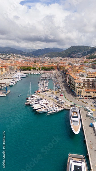 Fototapeta Aerial view of Nice, France, showcasing the vibrant port filled with luxury yachts and turquoise waters, with the city's colorful buildings and surrounding hills in the background