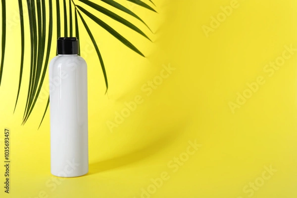 Fototapeta Shampoo in bottle and green palm leaves on yellow background. Space for text