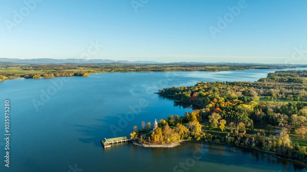 Obraz Aerial view of a scenic peninsula at Crown Point, surrounded by Lake Champlain’s calm waters, adorned with autumn trees and a historic monument, capturing vibrant fall colors and tranquility.
