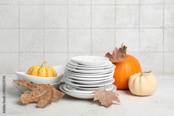 Fototapeta Stack of dishes with autumn decor and pumpkins on table against white tile background