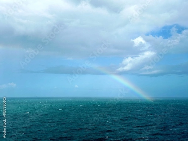 Fototapeta A clear rainbow in the middle of the ocean breaking through the clouds into the sea