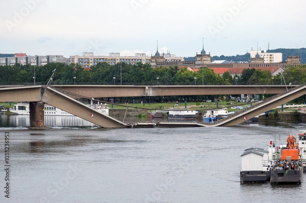 Fototapeta Blick auf die teileingestürzte Carolabrücke in Dresden, direkt am nächsten Morgen nach dem nächtlichen Einsturz vom Elbeufer aus, mit Maschinen, Gerät und und Bergungsschiffen – viel Copy Space