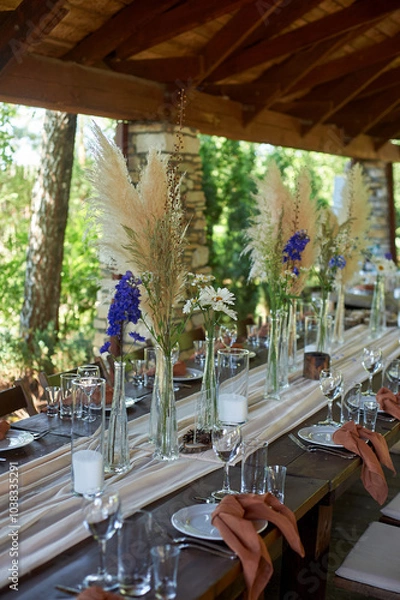 Fototapeta Wedding decoration. Floristics. Vessels with candles and bulk wax. Transparency and ease of design. Blue flowers and pampas.