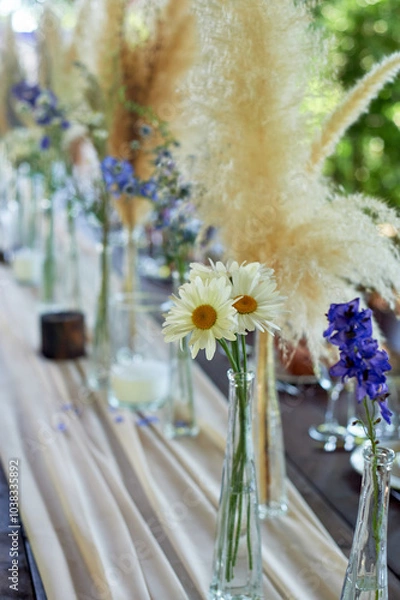 Fototapeta Wedding decoration. Floristics. Vessels with candles and bulk wax. Transparency and ease of design. Blue flowers and pampas.