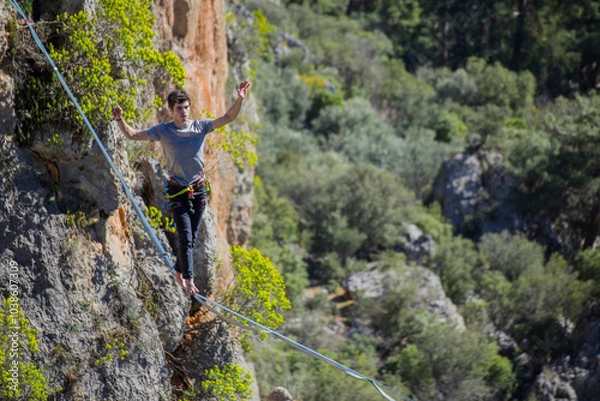 Obraz A tightrope walker walks along a cable stretched over a canyon.