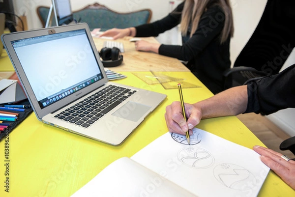 Fototapeta creative people from the company's marketing department work on defining a new product logo, drawing a sketch by hand and then refining it on the computer 