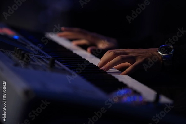 Fototapeta A striking close-up of a Black man's hands gracefully dancing over a keyboard, illuminated by cinematic lighting. The dark, moody atmosphere, combined with backlighting and a blurred background, creat