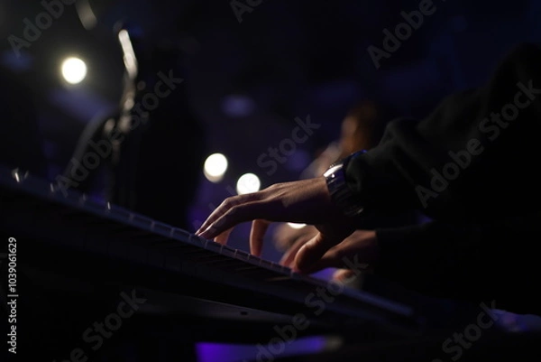Fototapeta A striking close-up of a Black man's hands gracefully dancing over a keyboard, illuminated by cinematic lighting. The dark, moody atmosphere, combined with backlighting and a blurred background, creat