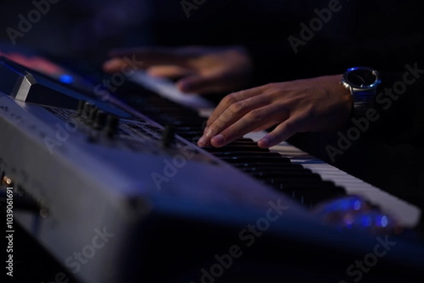 Fototapeta A striking close-up of a Black man's hands gracefully dancing over a keyboard, illuminated by cinematic lighting. The dark, moody atmosphere, combined with backlighting and a blurred background, creat