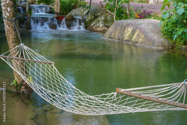 Obraz A peaceful hammock by a serene stream in nature, surrounded by lush greenery with sunlight filtering through the trees. The gentle stream flows beside the hammock, creating a calm and tranquil atmosph