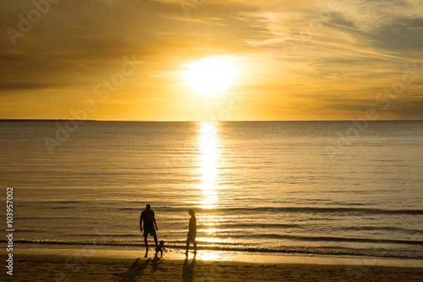 Fototapeta Young family in silhouette at the beach playing in the water, Darwin Australia