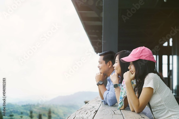 Fototapeta Parents and daughter sit with their hands under their chins looking at the mountain view outside from the balcony of their hotel accommodation during their vacation.Concept of family time and travel