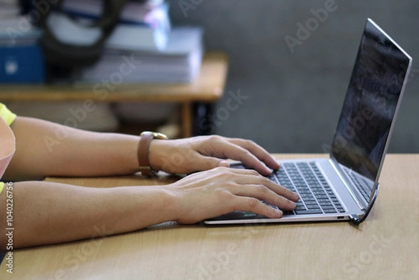 Fototapeta A woman is typing on a laptop, showing her dedication to her work in an environment full of textbooks.