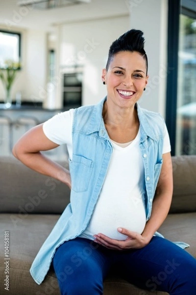 Fototapeta Portrait of pregnant woman sitting on sofa with and on stomach