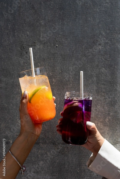 Fototapeta Two hands raising colorful drinks against a textured wall in a casual setting during daylight