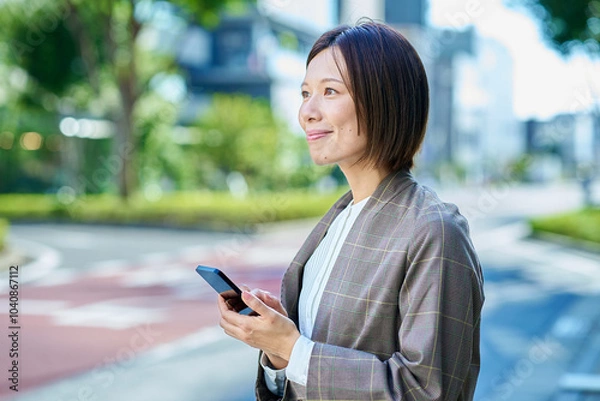 Fototapeta 屋外でスマートフォンを持つビジネスウーマン