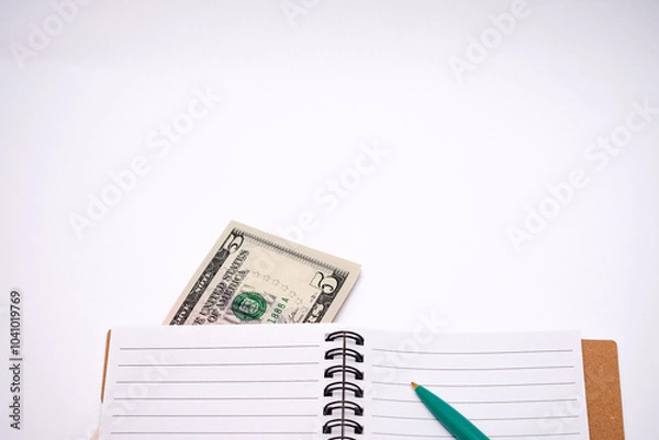 Fototapeta Five dollar bill is sitting on top of a spiral notebook