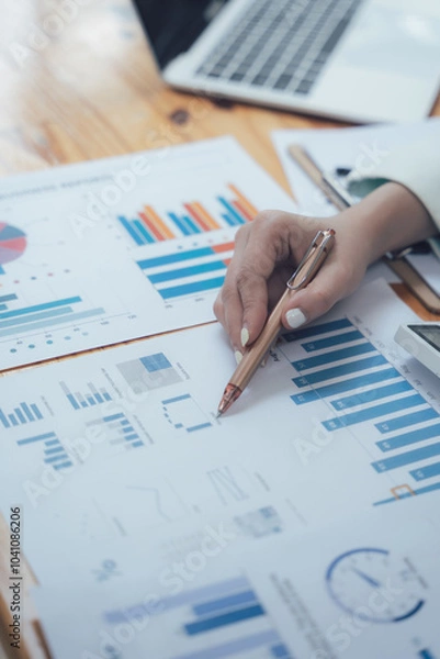 Obraz Analyzing the Data: Close-up of a hand pointing at a bar graph on a financial report, highlighting the crucial role of data analysis in business.  