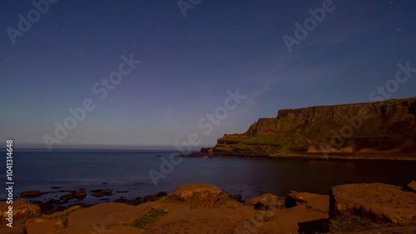 Fototapeta Giant's Causeway with the amphitheatre in the background under a clear night sky, faint green and red hues on the horizon
