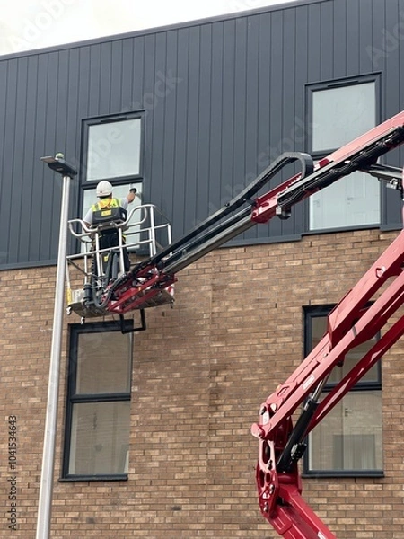Obraz window cleaner workers using a cherry picker on a construction site