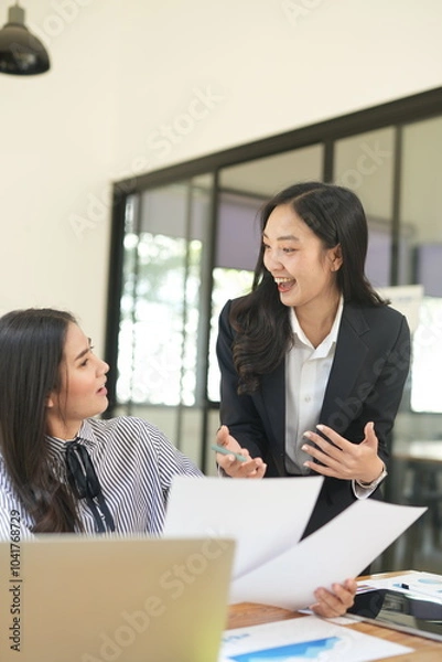 Obraz Group of happy Asian business people having a meeting at the office. Two women working together using modern laptops.