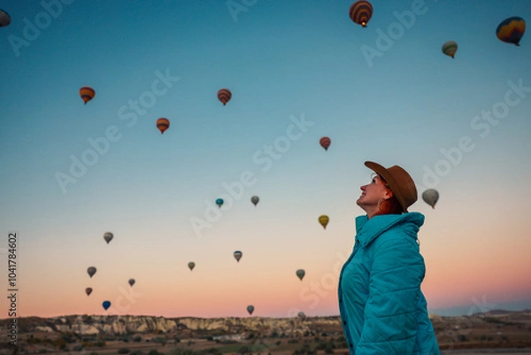 Fototapeta A woman marvels at colorful hot air balloons floating above Cappadocia at dawn capturing the enchanting beauty of the landscape