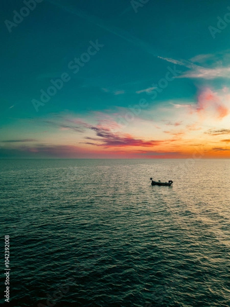 Fototapeta A small boat floats quietly under the colorful twilight sky over the Adriatic.