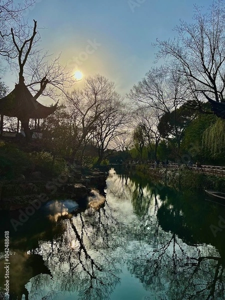 Fototapeta Tranquil River Scene with Reflections of Bare Trees and Setting Sun near a Traditional Pagoda