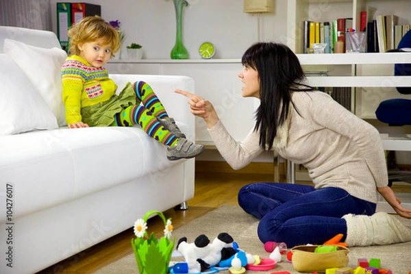 Obraz Young mother shouting to little daughter having made a mess with toys at home