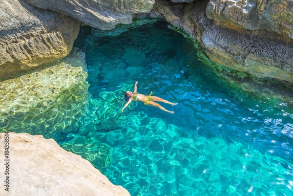 Fototapeta Young woman swimming between the rocks of Preveli beach in Crete