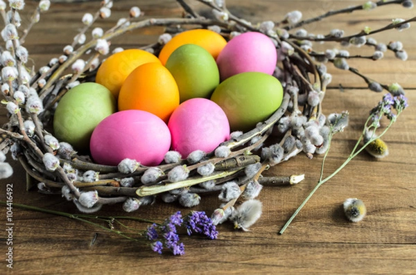Fototapeta Easter background, selective focus. Homemade hand painted colorful easter eggs in nest from willow branches close-up over retro wooden rustic background