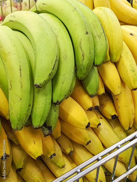 Fototapeta A bunch of green bananas and a bunch of yellow bananas are on the counter of a market, supermarket. The benefits of fresh fruits are a concept. Retail sale of fruits. Background. 