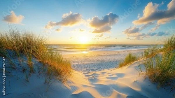Fototapeta A serene sunset over a beach, framed by sand dunes and grass.