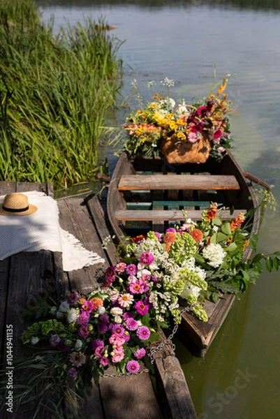 Fototapeta A serene boat adorned with vibrant flowers resting by a tranquil lake at midday, surrounded by lush greenery