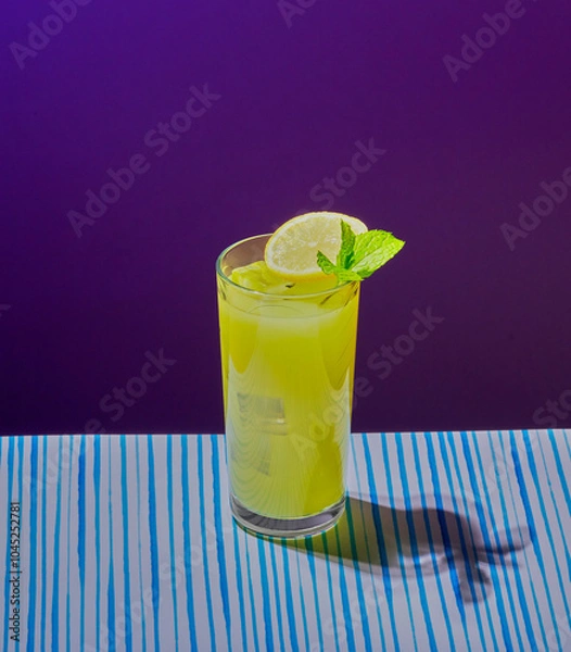 Fototapeta Yellow cocktail garnished with mint and a slice of lemon in a tall glass.