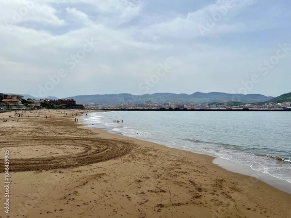 Obraz The beach at Getxo, Algorta, Bilao Spain.  View of the mountains in the background.  Unrecognisable people in the background laying on the beach and swimming.