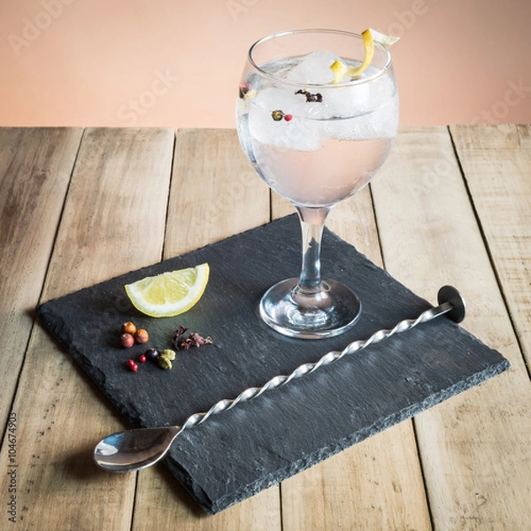 Fototapeta Gin Tonic with botanicals and bar spoon on wood table.